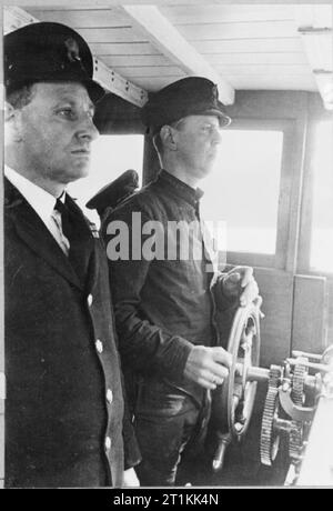 Ex-facteur fournit les canons- Formation de la marine marchande en Grande-Bretagne, 1942 Pour la première fois au cours de sa formation à la Royal Navy de l'Institut de formation pour les marins marchands, William Charles Piper prend le volant de sa propre. Le Premier Maître regarde son progrès. Cette photographie a été presque certainement prises sur le HMS GORDON à Gravesend dans le Kent. Banque D'Images