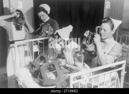 Gaz à percer à un hôpital de Londres- Masques à gaz pour les bébés sont testés, en Angleterre, en 1940, trois infirmières mettent leurs masques à gaz, tandis qu'un quatrième à l'infirmière assiste à des masques à gaz de deux bébés dans le lit d'en face d'elle. Les adultes ont été invités à prendre sur leur propre masque à gaz avant d'aider les enfants ou d'autres adultes avec les leurs. Banque D'Images