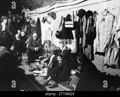 Une femme prépare un repas sur une cuisinière de Primus dans un abri anti-aérien sous les arches de chemin de fer dans le sud-est de Londres, 1940. Une femme prépare un repas dans un poêlon sur un réchaud Primus tandis que d'autres hébergeurs regardez sur dans ce refuge sous les arches de chemin de fer, quelque part dans le sud-est de Londres. De nombreuses pièces de vêtements et autres objets personnels, y compris chapeau et masque à gaz, les boîtes ont été suspendues à clous pour le murs blanchis à la chaux de l'abri. Cette photographie a probablement été prise en novembre 1940. Banque D'Images