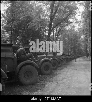 L'accumulation de l'invasion- Les préparatifs pour les débarquements du jour J, UK, 1944 Une ligne de camions de l'armée collecte attend le long d'une allée bordée d'arbres ou un chemin, quelque part en Grande-Bretagne. Ils seront bientôt recueillis par diverses unités et transportés à la deuxième face. Au premier plan, un mécanicien ATS peut être vu assis sur le passage de roue d'un des véhicules, son dos à la caméra. Un autre membre de l'ATS peut être vu marchant dans l'allée dans la distance. Banque D'Images