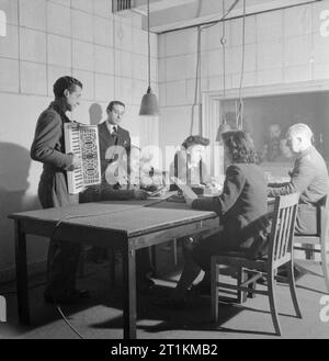 Prisonniers de guerre italien en Grande-Bretagne- la vie quotidienne dans un camp de prisonniers italiens, Angleterre, RU, 1945 à partir d'un studio de la BBC, prisonniers de guerre italien Aldo Maestro Morbio et Guido Leoni prendre part à l'émission hebdomadaire "Le Camp Journal" reflétant la vie à la N.144 camp travailleurs près de Londres. L'un des hommes est à jouer de l'accordéon. Deux femmes et plusieurs autres hommes peut également être vu assis autour de la table, au centre de laquelle se trouve la grande BBC Micro. Banque D'Images