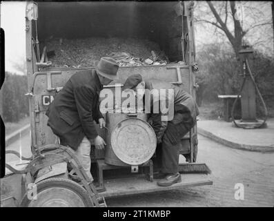 Les déchets de cuisine dans l'alimentation des bovins sur la récupération- British Home Front, 1942 travailleurs de récupération vider un bac est plein de restes de ménage dans un grand panier de poussière, quelque part en Grande-Bretagne. Banque D'Images