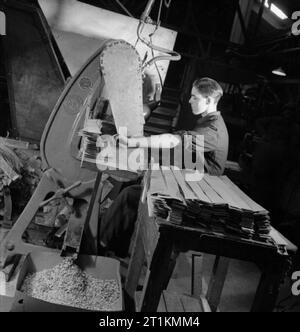 Lettre Dans Bullet- tournant en papier de récupération des cartouches de fusil, Angleterre, 1942 Un jeune travailleur rss des bandes de carton dans une machine qui fera beaucoup de perforation des trous dans la carte pour produire les petits disques nécessaires pour l'utilisation dans les balles et les cartouches. Les disques peuvent être vus à l'avant-plan, en descendant une chute de la poinçonneuse dans un grand bac. Banque D'Images