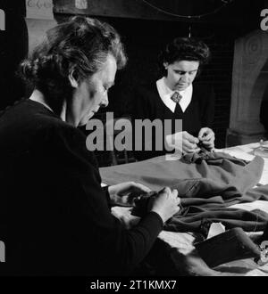 Les créateurs de mode Londres- le travail des membres de l'Incorporated Society of London Fashion Designers en temps de guerre, Londres, Angleterre, RU, 1944, dans les salles de la créatrice de mode Norman Hartnell à Londres, deux membres du personnel de s'asseoir à une table et le cloue ensemble un après-midi de jaquette. Banque D'Images