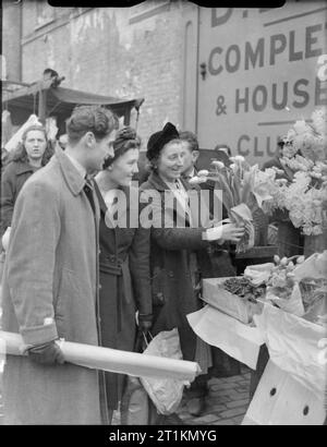 Londres au printemps de 1941- la vie quotidienne à Londres, Angleterre Un vendeur vend-fleur fleurs frais de Covent Garden à deux clients se rendant sur son stand à ce marché de Londres. Ainsi que les tulipes elle est tenue, jonquilles forment une grande partie de son stock. Banque D'Images