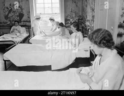 Hôtel particulier devient maison de maternité- La vie à Brocket Hall, Welwyn, Hertfordshire, 1942 nouvelles mères tricoter aussi ils sa convalescence dans un 'quartier' de Brocket Hall. Les murs de la chambre sont recouverts de papier peint chinois, qui, selon la légende originale, est très précieux. Dans l'arrière-plan, deux infirmières, les deux portant des masques chirurgicaux, tendent à un bébé dans un lit à côté du lit de sa mère. Banque D'Images