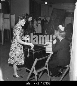 Les Londoniens enregistrer leur vote sur le jour du scrutin national, Holborn, Londres, Angleterre, Royaume-Uni, 5 juillet 1945 Une jeune femme place son bulletin de vote dans l'urne scellée dans le bureau de vote dans l'hôpital italien, Queen Square, Holborn. Trois bureaux de direction peut être vu assis au bureau. Dans l'arrière-plan, plus de personnes arrivent à exprimer leur vote. Les isoloirs sont tout juste visibles à gauche de la photographie. Banque D'Images