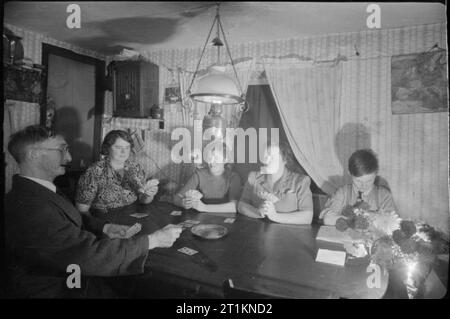 L'épouse de sergent au Moyen-Orient du signaleur ne travail- la vie comme un chemin de fer Signalwoman, Molland, Devon, Angleterre, RU, 1943 Signalwoman Daisy Cook, deuxième à partir de la droite, bénéficie d'un jeu de Newmarket à Furze Hill Farm, Molland, Devon. Cartes à jouer avec elle sont l'agriculteur Bill Petts, sa gouvernante Mme Ayre et Mme Ayre's daughter Phyllis. La lecture d'un livre sur le droit de la photographie est Bill Petts' 12 ans, petit-fils, Frank. Assis sur l'épaule de Phyllis est macaw, qui était un présent de M. Petts' fille, qui est une infirmière en Inde. Daisy est un séjour à Furze Hill Farm pour la durée de la guerre, ayant Banque D'Images