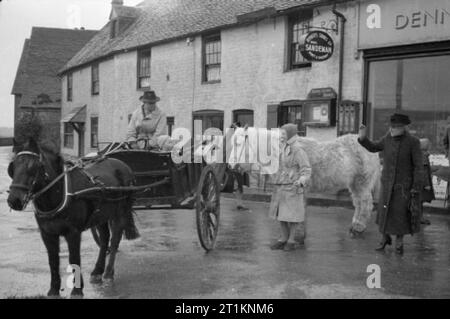 Mme clairon Goes To War- la vie quotidienne au doyen, Sussex, Angleterre, 1943 Mme clairon (droite) dit au revoir à Jimmy Gilbert, petit-fils du Major Harding, le village Squire, comme il se déplace avec son oncle dans un poney et piège. Mme clairon est debout à l'extérieur, de Dennett magasin du village. La légende originale membres qu'en raison des pénuries d'essence, le poney et le piège est maintenant une "vision commune en Grande-Bretagne". Banque D'Images