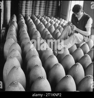 La production de munitions en Grande-Bretagne, 1940 lignes de bombes lourdes sont vérifiés pour les nombres à une fabrique d'armes, quelque part en Grande-Bretagne, 1940. L'homme travailleur de munitions est assis sur le haut de la bombes pour faire ses notes. Banque D'Images