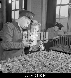 Service national de prévention des incendies sur la production de guerre Guerre- travailler dans un poste de pompiers, Londres, Angleterre, RU, 1943 à la caserne de pompiers dans l'East End de Londres, les hommes de la SNF produisent des unités de contrôle pour les radios de chasse de nuit. Mlle Rene Milner a venir de l'usine pour expliquer le processus de production pour les pompiers. Selon la légende originale, le poste d'incendie produit 300 unités par semaine. Banque D'Images