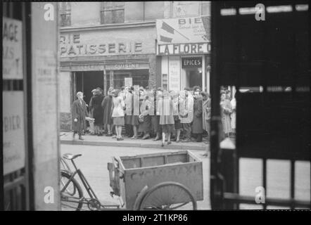 Paris, printemps 1945- la vie quotidienne dans Paris libéré, France, 1945 Un grand groupe de civils à l'extérieur des files d'une boulangerie-pâtisserie dans une rue, quelque part dans Paris. Il y a un grand nombre d'hommes dans cette file d'attente, qui est une grande différence de files d'attente similaire en Grande-Bretagne. Un garçon vient d'acheter ses deux baguettes. Dans l'avant-plan peut être vu un 'Cyclo-Taxi'. Banque D'Images