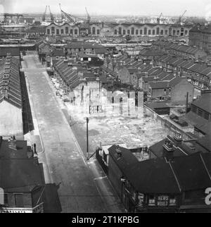 Curé- les travaux de la vicaire de St Mark's Church, Victoria Docks, Silvertown, Londres, Angleterre, RU, 1944 Vue d'un espace de Silvertown montrant une rue déserte, mais ensoleillé, avec un grand écart entre les maisons sur la droite, le résultat d'une bombe pendant le Blitz. Plusieurs chiens peuvent seulement être vu dans la route. En bas à droite de la photo, un papetier et du tabac shop peut être vu juste : il semble appartenir à J W Forrest. Dans le coin inférieur gauche est une succursale de la Banque Barclay's. Les quais peut être vu dans l'arrière-plan. Banque D'Images