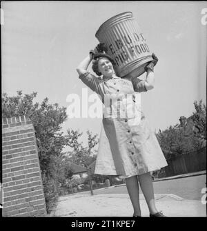 L'alimentation des porcs- Women's Voluntary Service collecte des déchets de cuisine récupérés, East Barnet, Hertfordshire, Angleterre, 1943 Un portrait en pied de Kathleen Kent, transportant un cochon bin sur son épaule, sur une rue ensoleillée pendant ses tournées quotidiennes. Kathleen est le chef de l'unité de collecte d'aliments porcs à East Barnet. Banque D'Images