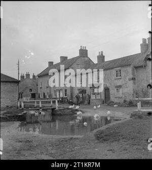 Village autonome- La vie à Hovingham, Yorkshire, octobre 1942 Une scène paisible d'un village anglais typique, montrant les canards sur l'eau de l'étang du village. Le bâtiment à droite de la photographie a un café. Un homme peut être vu à marcher en direction de l'duckpond. Banque D'Images