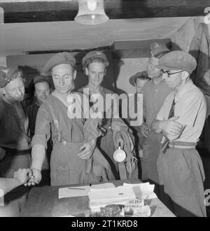 De travail des soldats sur le terrain, contribuant ainsi à la récolte, UK, juillet 1945 soldats sur pay parade en file d'attente pour leurs salaires à la fin d'une journée de travail contribuant à amener dans la récolte, quelque part en Grande-Bretagne. Inclus sont un homme d'un régiment de fusiliers du Lancashire Fusiliers, peut-être, recevoir son paiement, et plusieurs hommes de l'Artillerie royale. Selon la légende originale, « soldiers recevoir 1/ 6 pour chaque journée de travail en plus de leur paye de l'Armée'. Banque D'Images