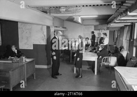 La jeune fille inconnue derrière la bataille de la mer- le travail de Women's Royal Naval Service, 1942 Une scène dans la salle des opérations chargé à bord du HMS EAGLET. Un message est remis au chef de cabinet par un messager de la Women's Royal Naval Service. Dans l'arrière-plan, les troglodytes "Traceur" attendre les ordres à la table de plotting. Banque D'Images