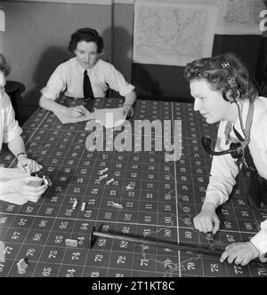 La jeune fille inconnue derrière la bataille de la mer- le travail de Women's Royal Naval Service, 1942 Wren Inconnu, portant des écouteurs et tube parlant, et un autre membre du WRNS regarder leur collègue supprime un 'U-Boat' à partir de la table de tracé dans la salle des opérations à l'Eaglet HMS. Banque D'Images