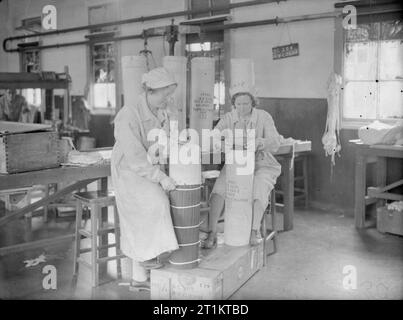 Les femmes derrière les canons- La production de munitions en Grande-Bretagne, 1940 Deux femmes représentent une charge de la cordite à une fabrique d'armes, quelque part en Grande-Bretagne. Banque D'Images