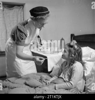 La formation des infirmiers et infirmières de district Queen- La formation des infirmières au Queen's Institute de soins infirmiers de district, Guildford, Surrey, Angleterre, RU, 1944 Un stagiaire District Nurse visite la maison d'une jeune fille qui se remet d'une pneumonie. La fille est assise dans le lit et est titulaire d'un tissu peluche en forme de canard. Banque D'Images