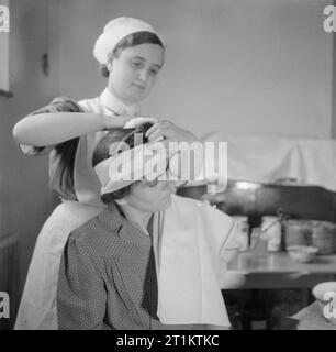 La formation des infirmiers et infirmières de district Queen- La formation des infirmières au Queen's Institute de soins infirmiers de district, Guildford, Surrey, Angleterre, RU, 1944 à l'Institut de la reine des sciences infirmières de district à Guildford, un stagiaire District Nurse bandages la tête d'une patiente. Banque D'Images