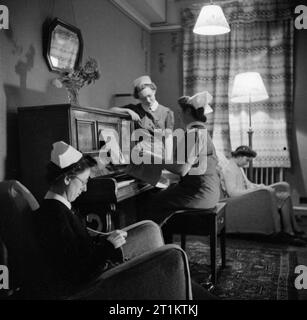 La formation des infirmiers et infirmières de district Queen- La formation des infirmières au Queen's Institute de soins infirmiers de district, Guildford, Surrey, Angleterre, RU, 1944 Après une dure journée de formation, stagiaire personnel infirmier de quartier vous détendre dans leur salon à la reine de l'Institut de soins infirmiers de district à Guildford. Certains sont la lecture ou la couture, assis dans les confortables fauteuils fournis, tandis que deux autres sont le choix d'un morceau de musique à jouer au piano. Banque D'Images