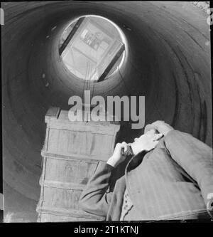 L'usine souterraine- la vie quotidienne dans une usine souterraine, probablement Printemps Carrière, Corsham, Wiltshire, Angleterre, 1942 Un ouvrier d'usine se trouve au fond d'un grand arbre rond comme une caisse est abaissée de plusieurs étages au-dessus de cette usine souterraine. Banque D'Images