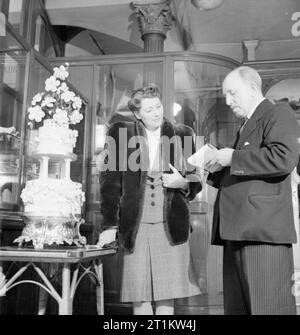 La vie de tous les jours- épouse de guerre en temps de guerre, Londres, mars 1943 Marcelle nouvellement recrutés Lestrange se penche sur un gâteau de mariage dans un magasin à Londres. L'assistant explique que l'effet de givrage est faite de papier de riz et en carton peint et se soulève pour révéler le vrai gâteau ci-dessous. Selon la légende originale : 'Le gâteau sous le parage est moins plein de groseilles qu'un gâteau d'avant-guerre et ne doit pas coûter plus de 35 cents la livre'. Banque D'Images