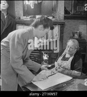 Enquête sociale de guerre- la collecte d'informations en temps de guerre La Grande-Bretagne, Royaume-Uni, 1944 Enquête sociale guerre Margaret Thomas intervieweur utilise un photomètre pour prendre une lecture légère dans la maison de Mme Bartram, dans Stepney Green, Londres. Cela fait partie d'une enquête réalisée pour le compte du ministère de la recherche scientifique et industrielle en tant qu'aide à la planification de l'après-guerre. L'objectif était d'examiner les niveaux d'éclairage dans les maisons et en interrogeant le dépliant, déterminer comment cela était adéquat et donc informer les besoins en éclairage, nouvellement construit des maisons d'après-guerre. Banque D'Images