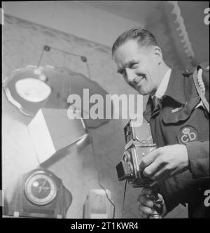 YMCA snapshots from Home- Civilian Photographers at Work, UK, 1944 un portrait du travailleur de la défense civile MR A E Moat alors qu'il prépare un plan dans la maison de Mme White à Edmonton. Selon la légende originale, « M. Moat prend toujours ses clichés à l'intérieur avec de la lumière artificielle, en utilisant des réflecteurs faits maison et des photofloods. Il essaie d'entrer dans ses images un coin familier, un fauteuil ou une cheminée pour rappeler au destinataire de la maison ». Une de ses lumières peut être vue juste derrière lui, entre l'horloge et le miroir de manteau. Banque D'Images