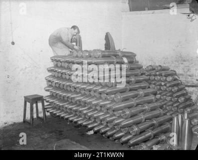 Au travail dans une usine de Shell en Angleterre, C 1940, un travailleur de munitions s'ajoute à un tas de produits finis, à une lourde coquille britannique usine. Banque D'Images