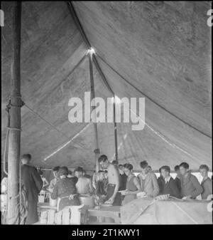 Youth Service Volunteers Help British Farmers- Agricultural Camp at Nunney Catch, Somerset, Angleterre, Royaume-Uni, 1943 garçons des Youth Service Volunteers font la queue pour leur souper, étant servis dans la grande tente de mess au camp agricole de Nunney Catch. Le gardien du camp, M. Dodd, et sa femme préparent le repas. Selon la légende originale, les garçons travaillant dans l'agriculture ont reçu des rations doubles par le gouvernement. Banque D'Images