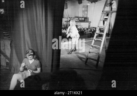 Ballet va à l'usine, de la danse et des animations organisées par le Conseil pour l'encouragement de la musique et des arts, en Angleterre, en 1943 une vue de la scène dans la cantine de l'usine, prises à partir de la 'ailes', montrant Sally Gilmour danser le rôle titre dans "Pierre et le loup". À travers les rideaux, les ouvriers d'usine peut être vu, de manger leur repas en regardant la performance, un avis à l'arrière-plan pour leur rappeler où mettre leurs couverts. Backstage, juste derrière le rideau, dans l'avant-plan de la photographie, est l'École Elizabeth, un autre danseur avec le Ballet Rambert, qui est l'un de reprisage Banque D'Images