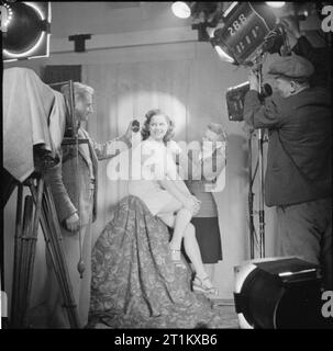 Naissance d'une étoile- la vie quotidienne pour l'actrice Muriel Pavlow, Angleterre, RU, 1945 L'actrice Muriel Pavlow sourire alors qu'elle est prête pour son photos publicitaires, pendant une séance photo, probablement à Welwyn Garden Studios, Hertfordshire. Photographe George Daley (à gauche) utilise un posemètre pour déterminer l'exposition correcte, tout en coiffure Elsie Bass donne la dernière touche les cheveux de Muriel. Un technicien peut être vue sur la droite, le réglage de l'éclairage. Banque D'Images