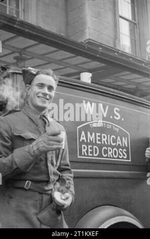 Cantine Blitz- les femmes du Women's Voluntary Service Exécuter une cantine mobile à Londres, Angleterre, 1941 Un ingénieur royal sourire pour la caméra en face de la WVS plateau voiture, donnés à la WVS par la Croix-Rouge américaine. Il tient une tasse de thé et une tarte aux fruits, qui sont ses 3 heures du thé l'après-midi, acheté de la WVS plateau voiture. Les Royal Engineers a été construire des ponts dans les cratères de bombes dans main throughfares et cette photographie a été prise quelque part à Londres en 1941. Banque D'Images