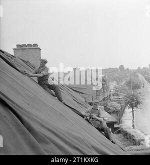 Blitz Repair Squad's Camp Londres- la vie quotidienne avec les équipes de réparation Blitz, Londres, Angleterre, RU, 1944 Les constructeurs de l'équipe de réparation 'Blitz' poser des bâches sur les toits des maisons pour protéger l'intérieur contre les éléments à la suite d'un V1, attaque qui a endommagé la plupart des maisons dans la rue. Ces constructeurs font partie d'une grande équipe qui ont voyagé à Londres, provenant de diverses régions du pays pour aider à réparer ces dommages. Banque D'Images