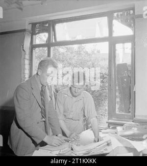 Blitz Repair Squad's Camp Londres- la vie quotidienne avec les équipes de réparation Blitz, Londres, Angleterre, RU, 1944 contremaître général J Wigley (Darlington) et de contremaître H Uttley regarder au-dessus des plans dans la 'Office' : le salon d'une bombe-maison endommagée, quelque part dans Londres. Ils font partie de l'équipe de réparation 'Blitz', une équipe de constructeurs qui sont venus à Londres, provenant de diverses régions du pays pour réparer les dégâts causés par des bombes volantes V1. Banque D'Images