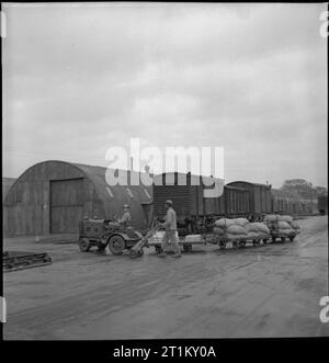 La Grande-Bretagne nous fourni le magasin de l'Armée- américains en Grande-Bretagne, 1943 Soldat Herbert M Mack (de 208, rue Gadson, Ocala, Floride) entraîne un petit camion tirant trois remorques contenant des sacs de café à un magasin de l'armée américaine, quelque part en Grande-Bretagne. Un autre GI pousse une brouette sac pendant qu'il marche à côté du chariot. Derrière eux, on peut voir le toit de ronde Romney huttes du camp et plusieurs voitures de fret ferroviaire, qui ont procédé à partir de marchandises autour de la Grande-Bretagne au camp. Arrivée des marchandises par rail et par route. Banque D'Images