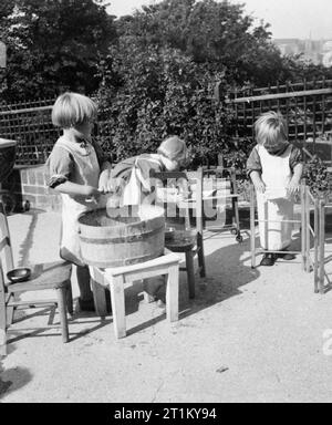 Un modèle d'école maternelle - le travail de la Terre Tarner Nursery School, Brighton, Sussex, Angleterre, RU, 1944 jeunes filles apprennent par le jeu à l'air libre à terre Tarner école maternelle. Une fille se lave les habits de poupée dans un bain à remous en bois, tandis qu'un autre est accroché sur un vêtements airer au soleil pour sécher. Derrière eux une troisième fille est à l'aide d'un petit mangle à essorer les vêtements. Banque D'Images