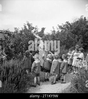 Un modèle d'école maternelle - le travail de la Terre Tarner Nursery School, Brighton, Sussex, Angleterre, RU, 1944 pour le thé l'après-midi, les enfants à terre Tarner Nursery School à Brighton chaque choisir Apple à partir de l'arbre dans l'ensoleillée jardin de l'école. Lorsqu'ils ont insisté sur le morceau de fruit qu'ils veulent manger, le jardinier femelle atteint jusqu'à le prendre pour eux. Banque D'Images