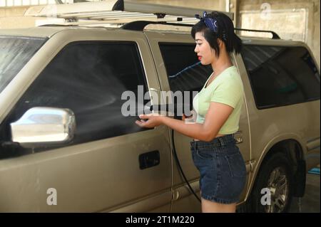 Jolie femme asiatique pulvérisant de l'eau pour laver la voiture. Banque D'Images