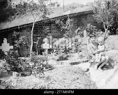 La flotte britannique du Pacifique 1944-1945 Juan et Dennis Clark, peu d'internés du camp Stanley, Hong Kong, s'asseoir à côté de la tombe de leur petit frère Anthony, qui est né le 2 décembre 1942, dans le camp, et sont morts de malnutrition trois semaines plus tard. Père était un policier eurasien à Hong Kong quand les Japonais sont entrés dans la ville et les internés. Les enfants avaient une partie spéciale du cimetière jouxtant le camp. Banque D'Images