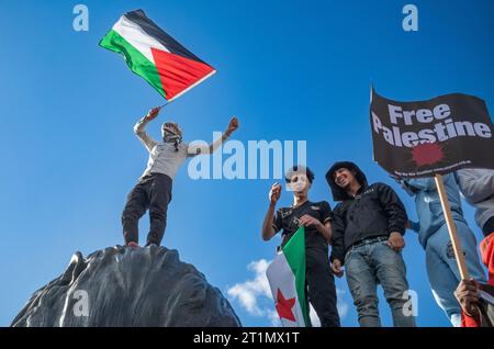 Londres, Royaume-Uni. 14 octobre 2023 : des manifestants pro-palestiniens se tiennent debout sur la statue du lion géant sur la place Trafalgar tenant un drapeau palestinien en soutien à la Palestine et contre les attaques israéliennes sur Gaza. Banque D'Images