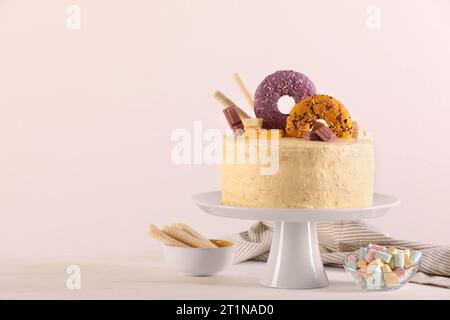 Délicieux gâteau décoré avec des bonbons, des rouleaux de gaufrette et des guimauves sur une table en bois blanc, espace pour le texte Banque D'Images