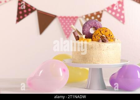 Délicieux gâteau décoré avec des bonbons et des ballons sur la table en bois blanc, espace pour le texte Banque D'Images