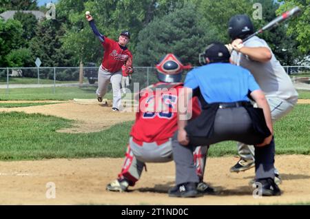 Spring Grove, Illinois, États-Unis. Lanceur lâchant un terrain à un batteur en attente pendant un match de baseball amateur masculin dans la banlieue de Chicago. Banque D'Images