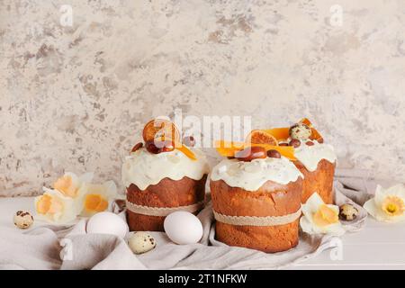 Gâteau de Pâques avec des narcisses et des œufs sur une table en bois blanc près du mur grunge beige Banque D'Images