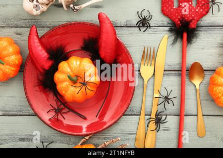 Réglage de table d'Halloween avec squelette, fourche de diable rouge et cornes sur fond en bois de couleur, closeup Banque D'Images