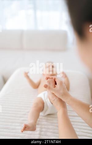 Plan de mise au point sélective verticale d'une femme thérapeute méconnaissable médecin faisant de la gymnastique et du massage des pieds à un adorable bébé en bas âge. Banque D'Images