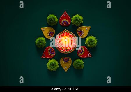 Lampe en argile diya lit pour célébrer pour le festival Diwali avec des objets de décoration colorés et des fleurs vertes sur fond vert foncé. Banque D'Images